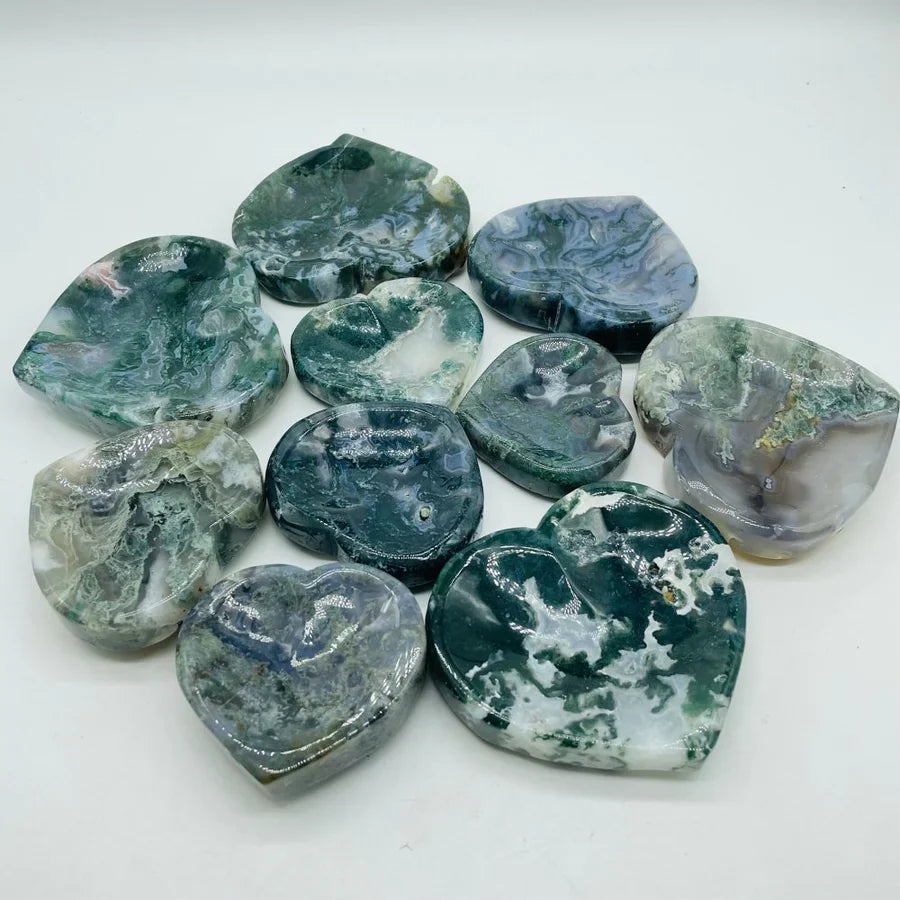 A group of polished heart-shaped gemstone pendants with natural marbled patterns in shades of green, gray, white, and blue, arranged on a plain white background.